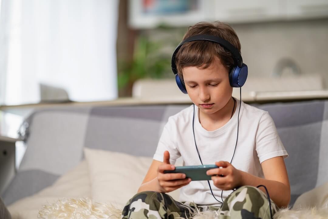 boy with headphones smartphone his hands is sitting sofa playing