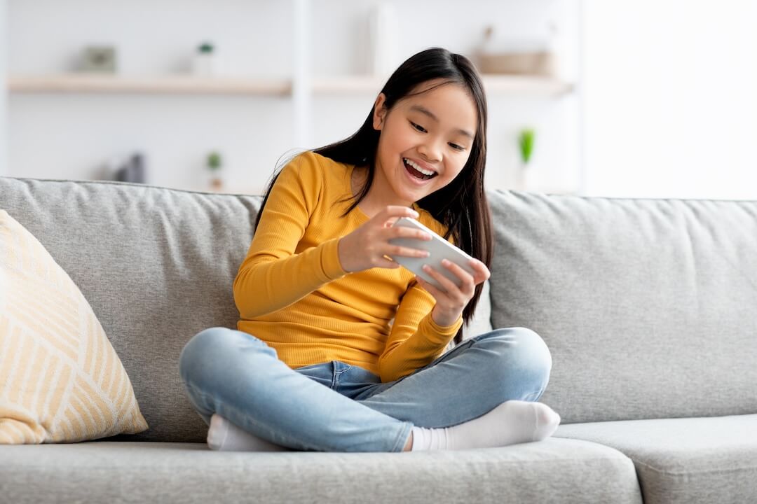 Young girl playing on handheld on couch